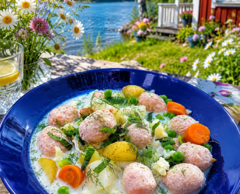 Siskonmakkara kesäkeitto sinisellä lautasella, mukana Wurstin siskonmakkarapalleroita, uusia perunoita, porkkanoita ja herneitä.