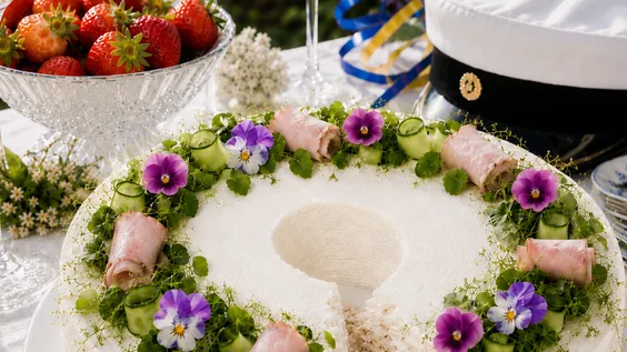 Kukkasin ja kinkkurullin koristeltu kinkkuvoileipäkakku kesäisessä valmistujaisjuhlapöydässä.